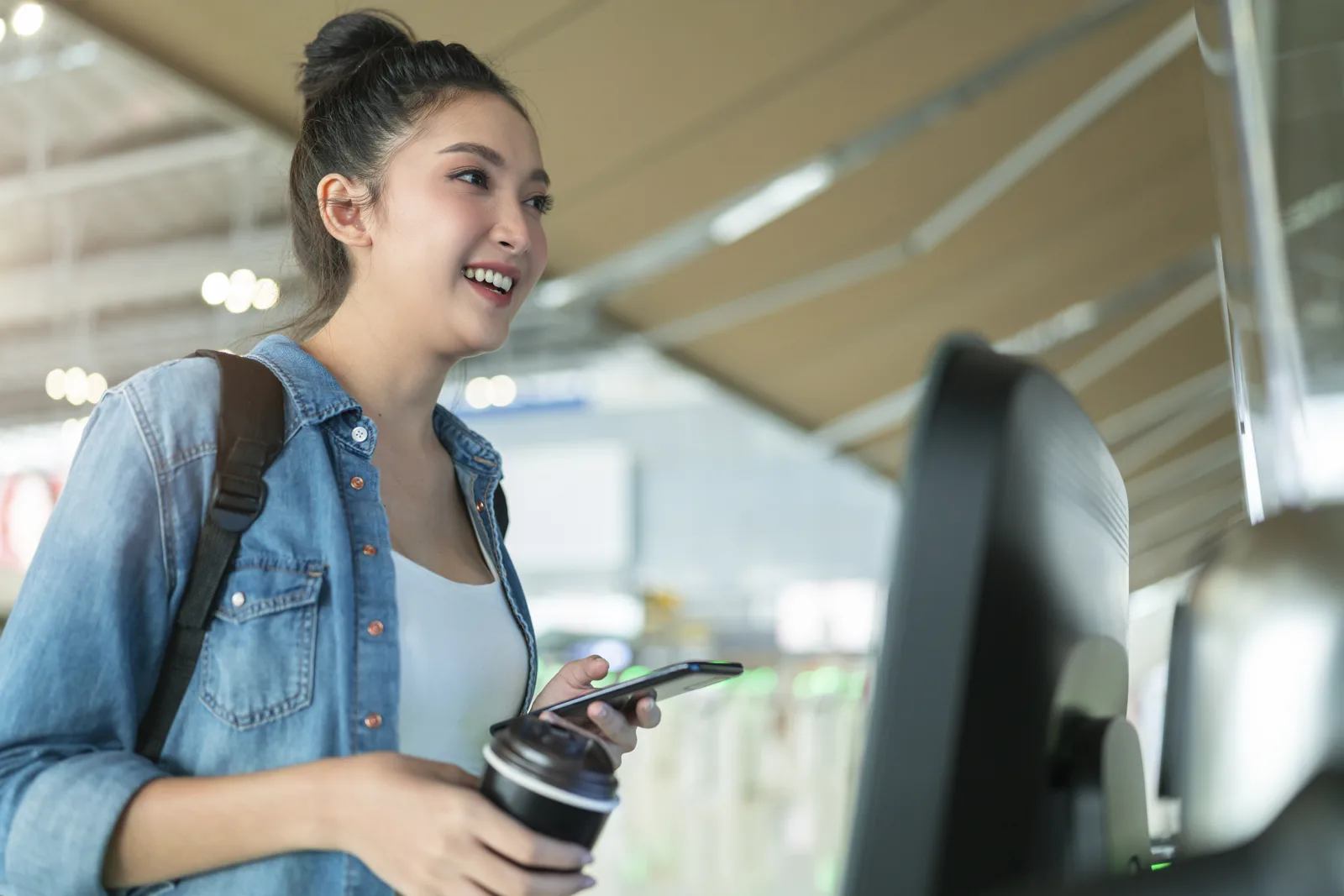 Traveler using a mobile phone at an airport self-check-in kiosk