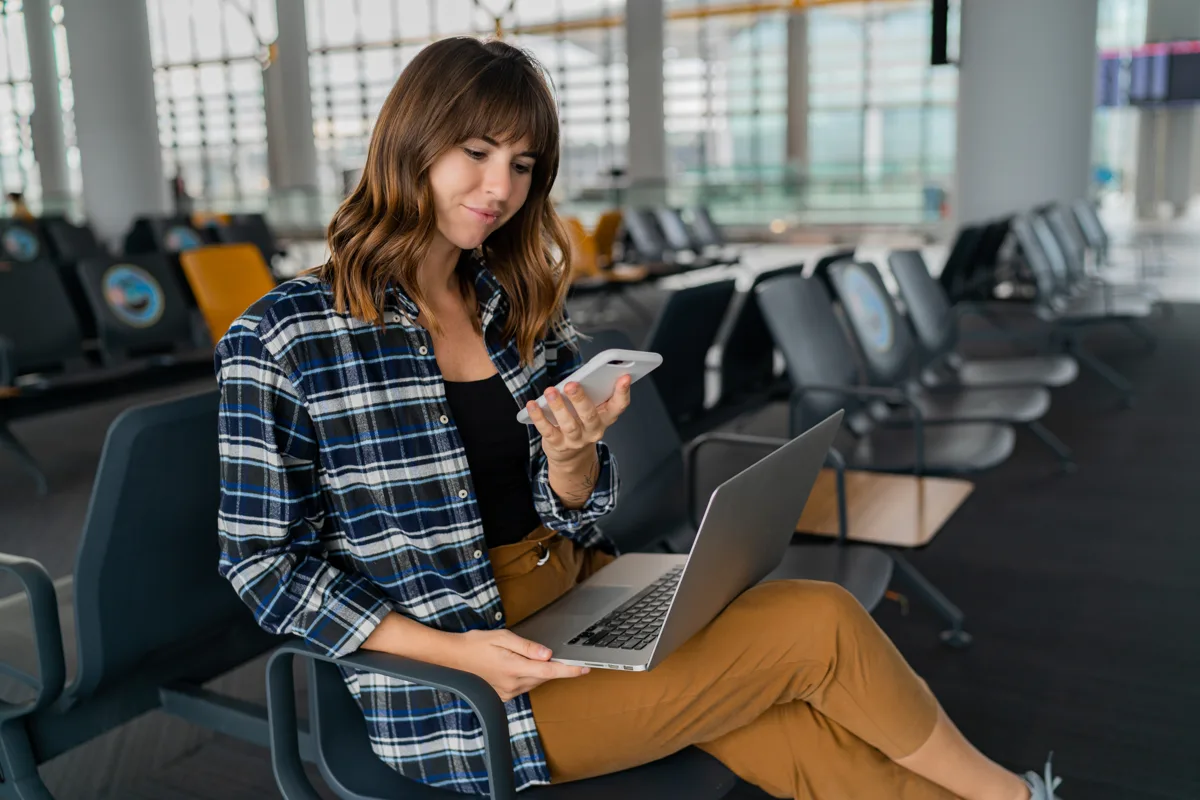 Traveler checking a flight itinerary on laptop and phone at the airport gate