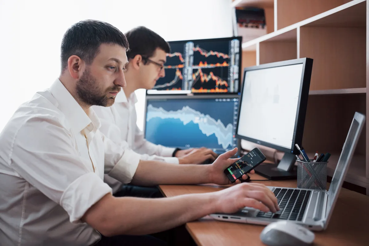Banking IT team reviewing trading data across multiple monitors and mobile