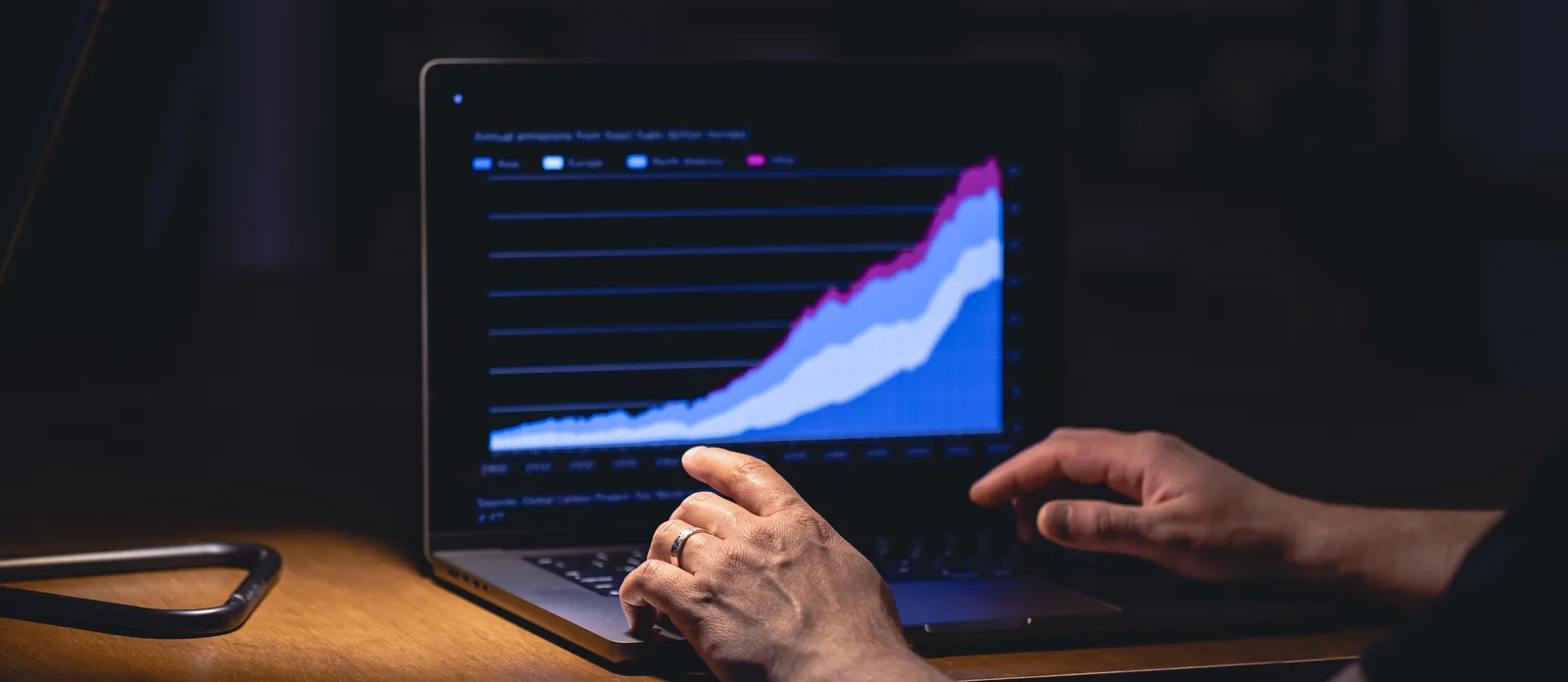 Hands typing on a laptop showing a financial trading dashboard chart at night